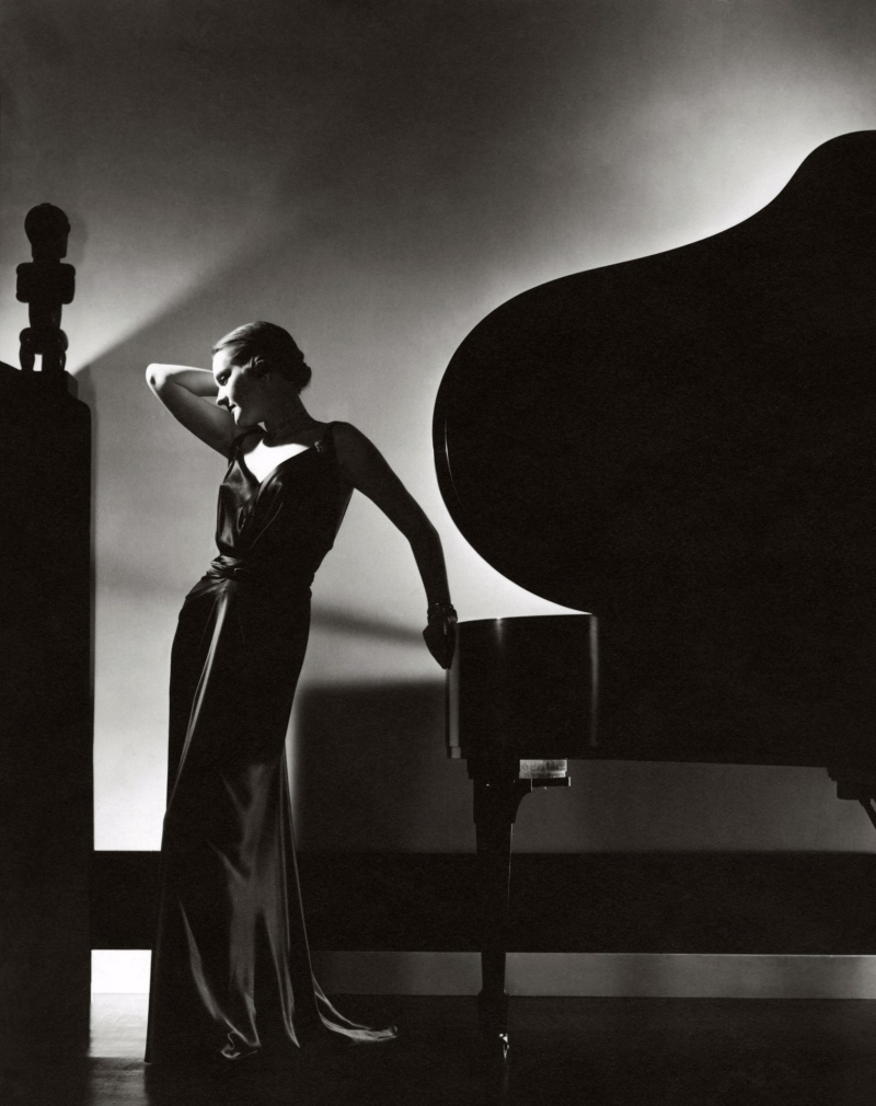 Margaret Horan, wearing a fitted sleeveless black satin dress with V-neckline by Jay-Thorpe, and standing beside a Steinway piano with a small African sculpture silhouetted in the upper left *** Local Caption *** Margaret Horan;